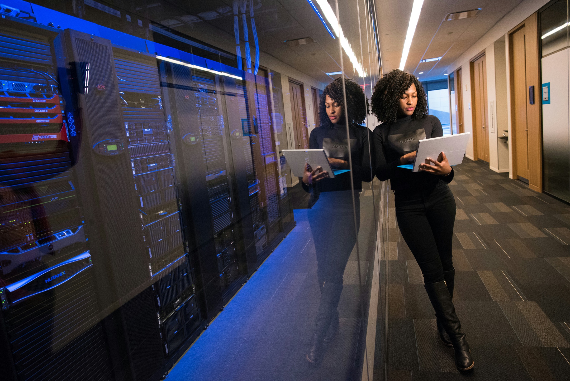 IT professional using a laptop in a blue-lit server room representing computers and servers